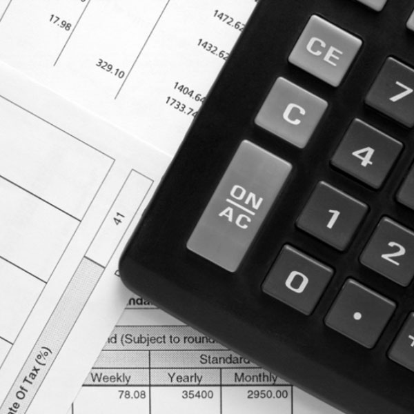 Black and white image of a calculator on top of many tax forms and documents.