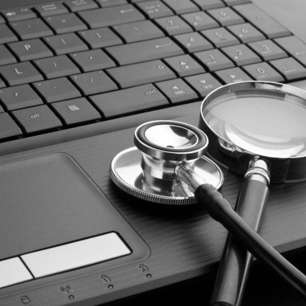 Black and white image of a magnifying glass and a stethoscope on a laptop.