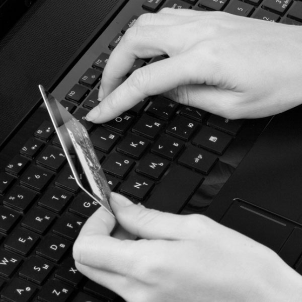Black and white image of a person hand's holding a credit card and typing on a computer keyboard.