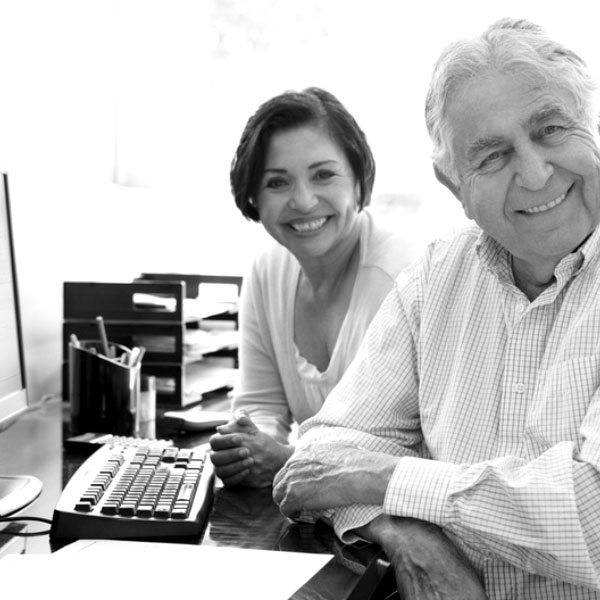 Black and white image of two people looking and smiling while sitting at an office computer.