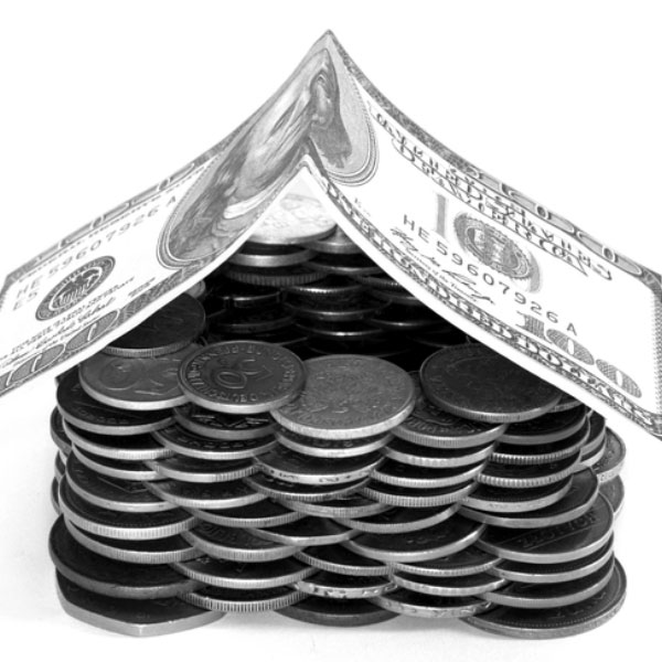 Black and white image of a pile of coins and a 100 dollar bill shaped to look like a house resting on top.