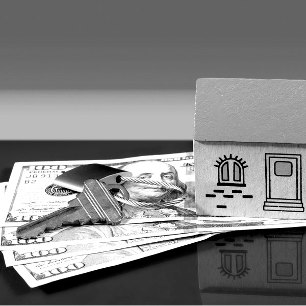 black and white image of Keys sitting on a table with several hundred-dollar bills and a mini home to symbolize home and mortgage loans.