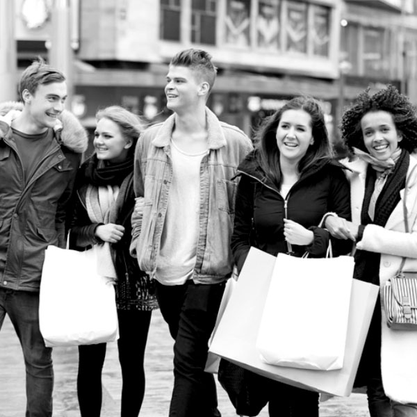 black and white image of a group of 5 people smiling and carrying shopping bags.