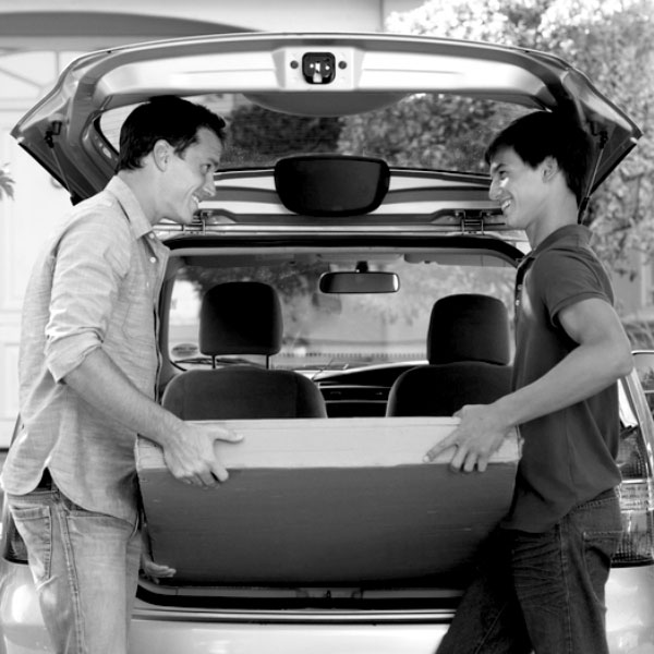 black and white image of a father helping his son move things into his new car.