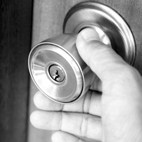 Black and white image of a person putting their hand on a doorknob