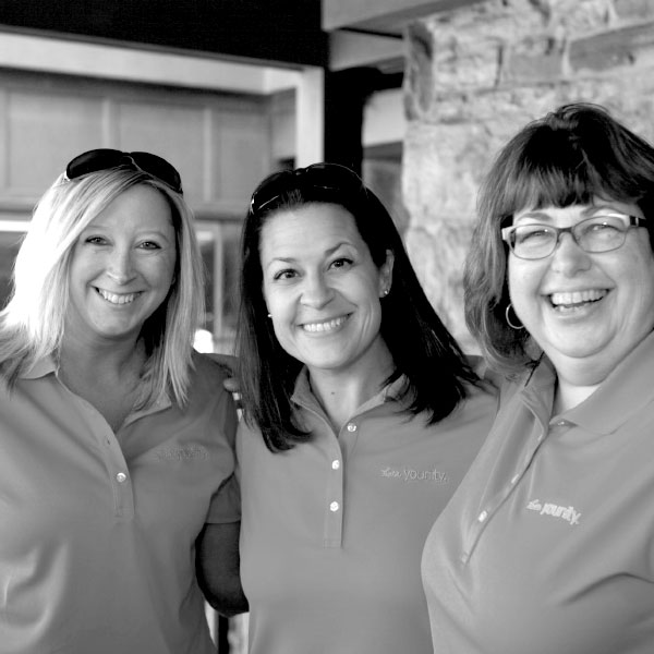 Black and white image of three Diamond team members smile together outside.