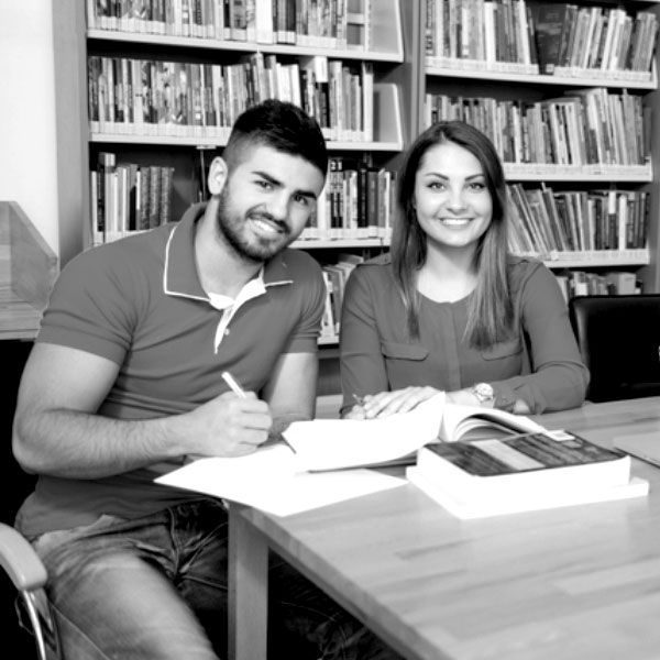 Black and white image of two students sitting at a table in a library.