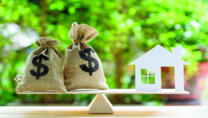 A balanced scale with money on one side and a house item on the other. Represents home equity loans.