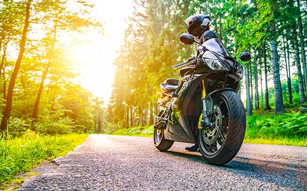 A motorcycle on a paved road in the middle of the woods.